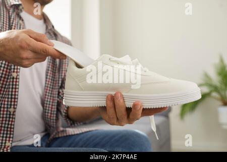 Giovane uomo mette nuove solette ortopediche all'interno delle sue comode scarpe ortopediche bianche Foto Stock