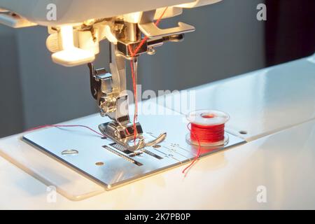 Macchina cucitrice piede e ago con rocchetto di filo rosso. Primo piano delle parti di lavoro della macchina cucitrice Foto Stock