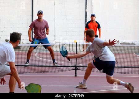 Un gruppo di millenial maschi bianchi gioca a pickleball su un campo da basket con doppio pickleball e strisce di campo da basket a Manhattan, New York City Foto Stock