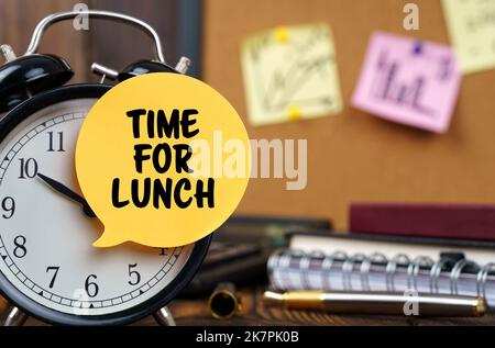 Concetto aziendale. Le sveglie hanno un adesivo con la scritta - TEMPO PER IL PRANZO. Ci sono articoli per ufficio sullo sfondo in un backgrou sfocato Foto Stock