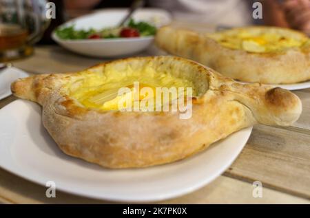 Belle torte khachapuri aperte con uova e burro su un piatto bianco. Tradizionale piatto Georgiano. Foto Stock