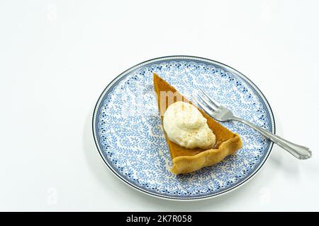 Pezzo isolato di torta di zucca arancione con panna montata su piatto con fondo bianco. Foto Stock