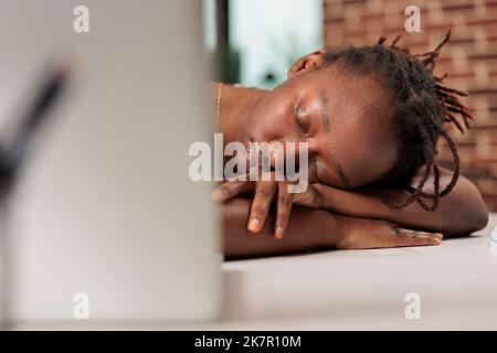 Stressato telelavoro che dorme sul tavolo durante il giorno, assonnato superlavoro freelance, burnout professionale. Studente stanco sdraiato sulla scrivania, vista ravvicinata sul viso, impiegato esausto in pausa Foto Stock