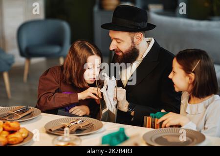Ritratto della famiglia ebraica moderna che condivide regali con i bambini al tavolo da pranzo in un ambiente accogliente casa Foto Stock