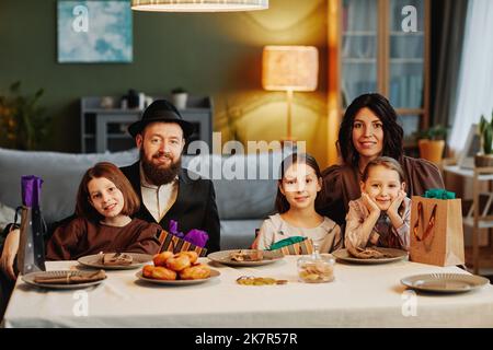 Ritratto della moderna famiglia ebraica guardando la macchina fotografica mentre si siede al tavolo da pranzo in un ambiente accogliente casa Foto Stock