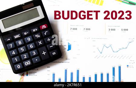 Blocco note con testo BUDGET 2023, occhiali, graffette, calcolatrice bianca e penna su un desktop, vista dall'alto Foto Stock