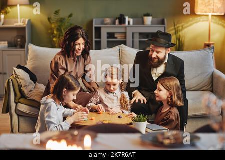 Ritratto della famiglia ebraica moderna che gioca tradizionale gioco dreidel in un ambiente accogliente casa Foto Stock