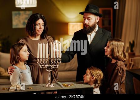 Ritratto di famiglia ebraica ortodossa illuminazione menorah candela durante Hanukkah celebrazione a casa Foto Stock