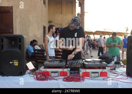 DJ maschile con giradischi, mixer e altoparlanti professionali forniscono musica e atmosfera ad una fiera d'arte alla moda a Dubai, negli Emirati Arabi Uniti. Evento estivo all'aperto durante il fine settimana di sole. Foto Stock