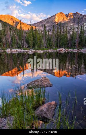 Il monte Ypsilon e il monte Chiquita si riflettono nelle acque calme del lago Chipmunk, con la prima luce dell'ora d'oro nel Parco Nazionale delle Montagne Rocciose Foto Stock