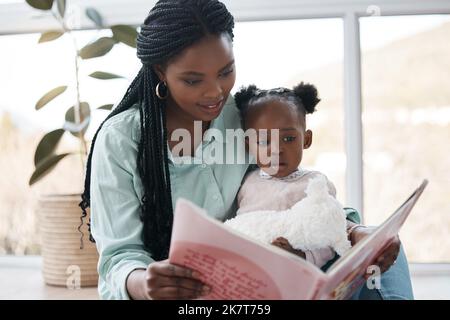 La maternità è un viaggio magico. una donna che legge un libro a sua figlia mentre si siede a casa. Foto Stock