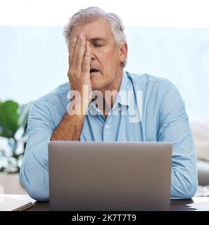 Argh, dai. un uomo maturo che si siede da solo e si sente stressato mentre usa il suo computer portatile per lavorare da casa. Foto Stock