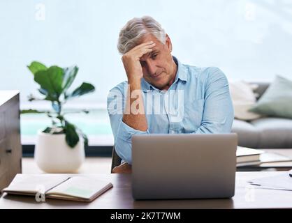 Perché continuo a fare lo stesso errore. un uomo maturo che si siede da solo e si sente stressato mentre usa il suo computer portatile per lavorare da casa. Foto Stock