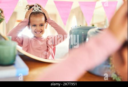 Non lasciare mai cadere la corona. una bambina che mette una corona nello specchio a casa. Foto Stock