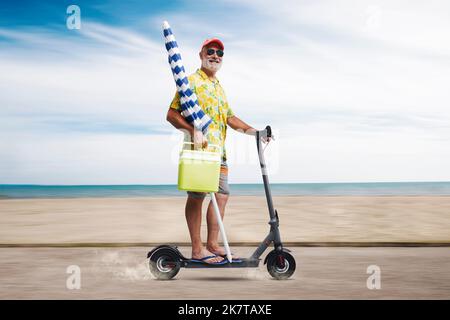 Divertente uomo anziano che tiene un ombrellone e guida uno scooter elettrico, sta andando in spiaggia Foto Stock