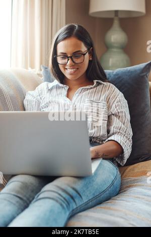 Trascorrere un po' di tempo online. una giovane donna attraente che usa il suo laptop mentre si rilassa su un divano a casa. Foto Stock