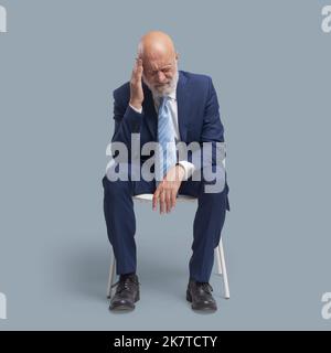 Uomo anziano seduto su una sedia, sta avendo un mal di testa cattivo Foto Stock