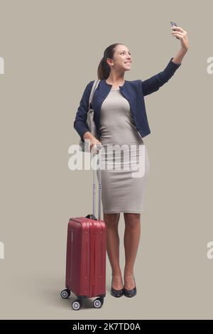 Giovane donna d'affari che viaggia e utilizza uno smartphone, sorride e prende un selfie Foto Stock