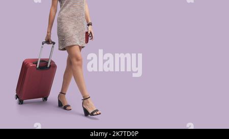 Giovane donna alla moda che viaggia da sola, cammina e tira una valigia per il carrello Foto Stock