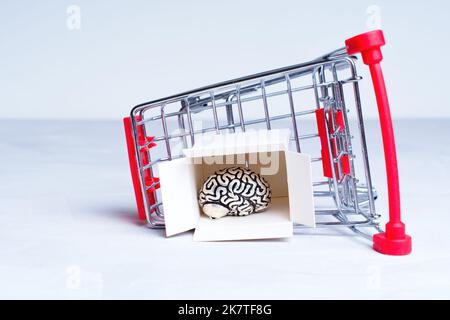 Primo piano di un carrello capovolto con un cervello umano all'interno di una scatola di spedizione aperta isolata in grigio. Concetto creativo di shopping terapia. Foto Stock