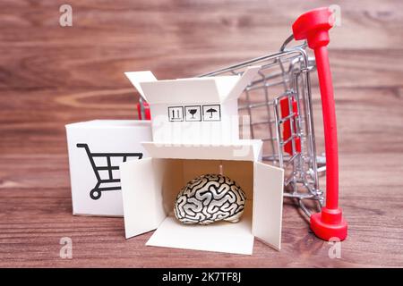 Carrello della spesa in miniatura rovesciato con piccole scatole di spedizione e cervello umano su uno sfondo di legno. Concetto di fornitura di tecnologia creativa. Foto Stock