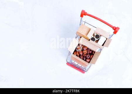 Chicchi di caffè e tazze di caffè arrosto in piccole scatole di spedizione caricate in un carrello a spinta miniaturizzato isolato su uno sfondo neutro con spazio per le copie. Foto Stock