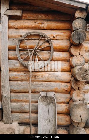 Un vecchio muro di legno di una casa nel villaggio e antiche ruote cart, utensili, ecc Foto Stock