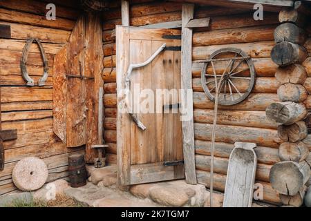 Un vecchio muro di legno di una casa nel villaggio e antiche ruote cart, utensili, ecc Foto Stock