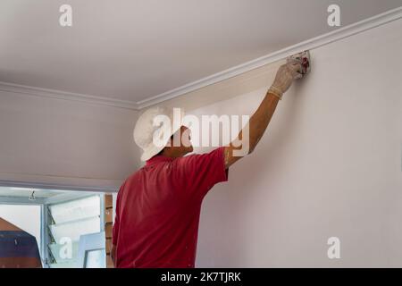 Uomo che dipinge la parete con rullo di bordo di vernice. Home ristrutturazione fai da te progetto. Foto Stock