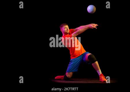 Ritratto dinamico dell'allenamento maschile con palla isolata su sfondo scuro in luce al neon. Sport, palestra, sport di squadra, sfide Foto Stock