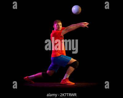 Ritratto dinamico dell'allenamento maschile con palla isolata su sfondo scuro in luce al neon. Sport, palestra, sport di squadra, sfide Foto Stock