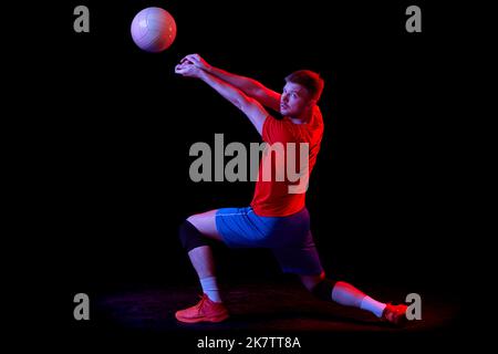 Ritratto dinamico dell'allenamento maschile con palla isolata su sfondo scuro in luce al neon. Sport, palestra, sport di squadra, sfide Foto Stock