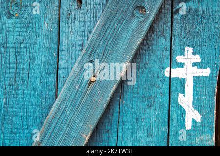 Croce cristiana ortodossa disegnata di vernice bianca su vecchia porta di legno blu. Sagome del simbolo del crocifisso. Cristianesimo sfondo religioso. Russo Foto Stock
