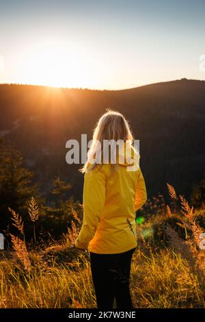 Donna con giacca gialla che gode di vista al tramonto sulle montagne durante le escursioni. Avventura nella natura Foto Stock
