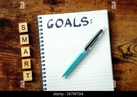 Concetto Smart Goals. Un blocco note con la parola manoscritta, per scrivere un piano o una lista, sopra la testa piatta stendere sparato su una scrivania di legno Foto Stock