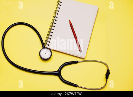 Tutto ciò che un medico ha bisogno di fare una diagnosi. Studio shot di uno stetoscopio e di un notebook su sfondo giallo. Foto Stock