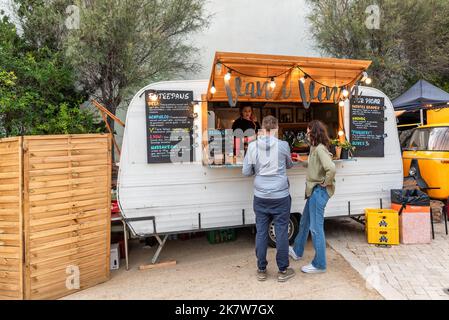 SITGES, BARCELLONA, SPAGNA - 08 OTTOBRE 2022: Giovane coppia che acquista cibo e bevande in una carovana abilitato per la vendita di fast food per la strada Foto Stock