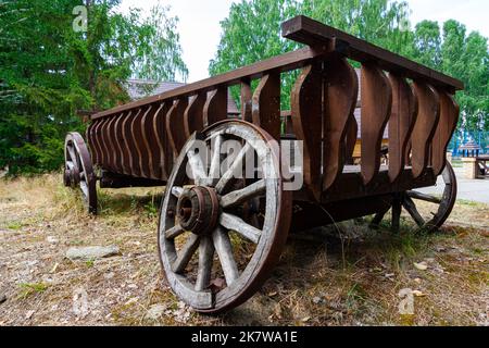 Un vecchio carrello rotto in legno con ruote si trova in natura nel villaggio in una giornata di sole d'estate. Il ferro è arrugginito. Primo piano. Orizzontale Foto Stock