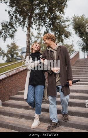 donna compiaciuta e uomo rosso con ombrello scendendo scale nel parco, immagine stock Foto Stock