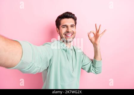 Selfie closeup cadre di attraente ragazzo che mostra un segno di okey toothy fascio sorridere buon lavoro blogger lifestyle canale youtube isolato sul colore rosa Foto Stock