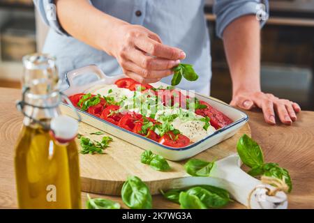 Dall'alto di raccolto anonimo femmina in abiti casual decorazione fresco caprese con basilico in ceramica piatto da portata posto su tagliere di legno vicino Foto Stock