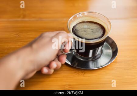 Caffè nero holdign mano su tavolo di legno. Foto Stock
