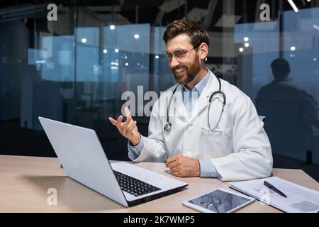 Esperto medico maturo che lavora a distanza, uomo anziano in abito medico che lavora online consulenza pazienti all'interno di clinica moderna, medico che utilizza il computer portatile per la videochiamata online. Foto Stock