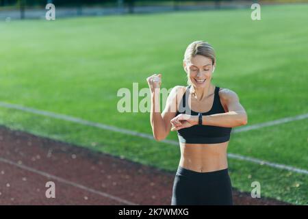 Soddisfatto del risultato dell'allenamento e della corsa, l'atleta guarda l'orologio intelligente, la bionda tiene la mano e celebra la vittoria. Foto Stock