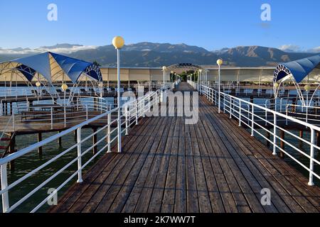 Riva nord del lago Issyk-Kul e vista sul molo e le alte vette di Tien Shan, Kirghizistan Foto Stock