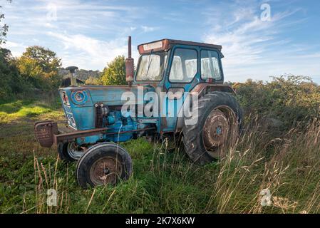 Vecchio trattore blu arrugginito seduto in un campo Foto Stock