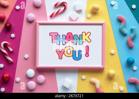 Testo grazie in cornice su carta colorata stratificata. Dolci assortiti, dolciumi, cioccolatini e caramelle intorno alla cornice. Piano di giacitura, vista dall'alto. Foto Stock