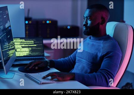 Ritratto del software engineer che scrive il codice sul posto di lavoro in luci al neon Foto Stock