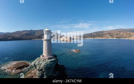 Andros Island. Grecia. Il faro di pietra su una vista aerea di roccia drone. Chora città e paesaggio roccioso Cicladi. Cielo blu e mare Foto Stock