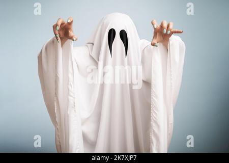 Concetto di Halloween. Un fantasma bianco con occhi neri, realizzato da un lenzuolo su sfondo blu Foto Stock